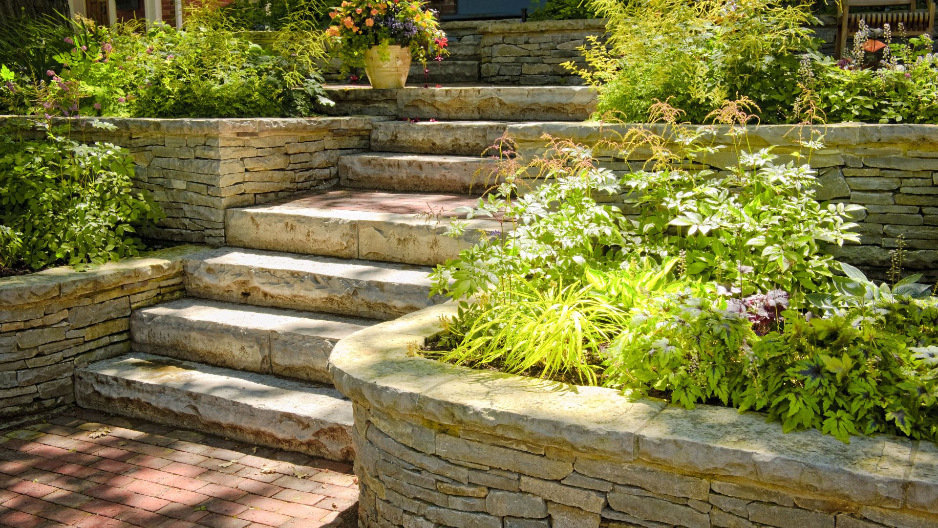 Stone garden steps with lush greenery, flowering plants, and landscaped retaining walls.