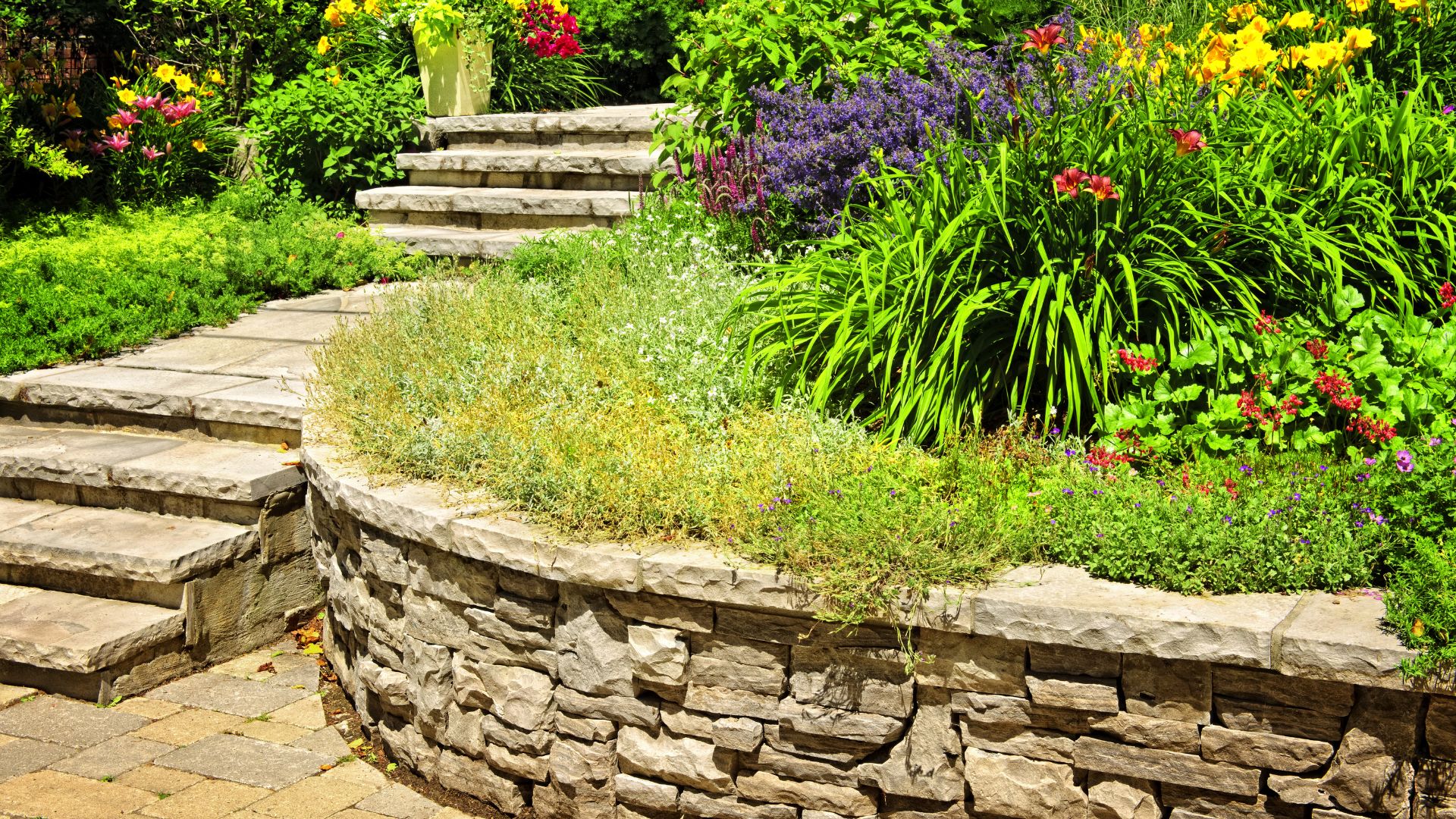 Vibrant garden with stone steps, pathways, and colorful flowers blooming around lush greenery.