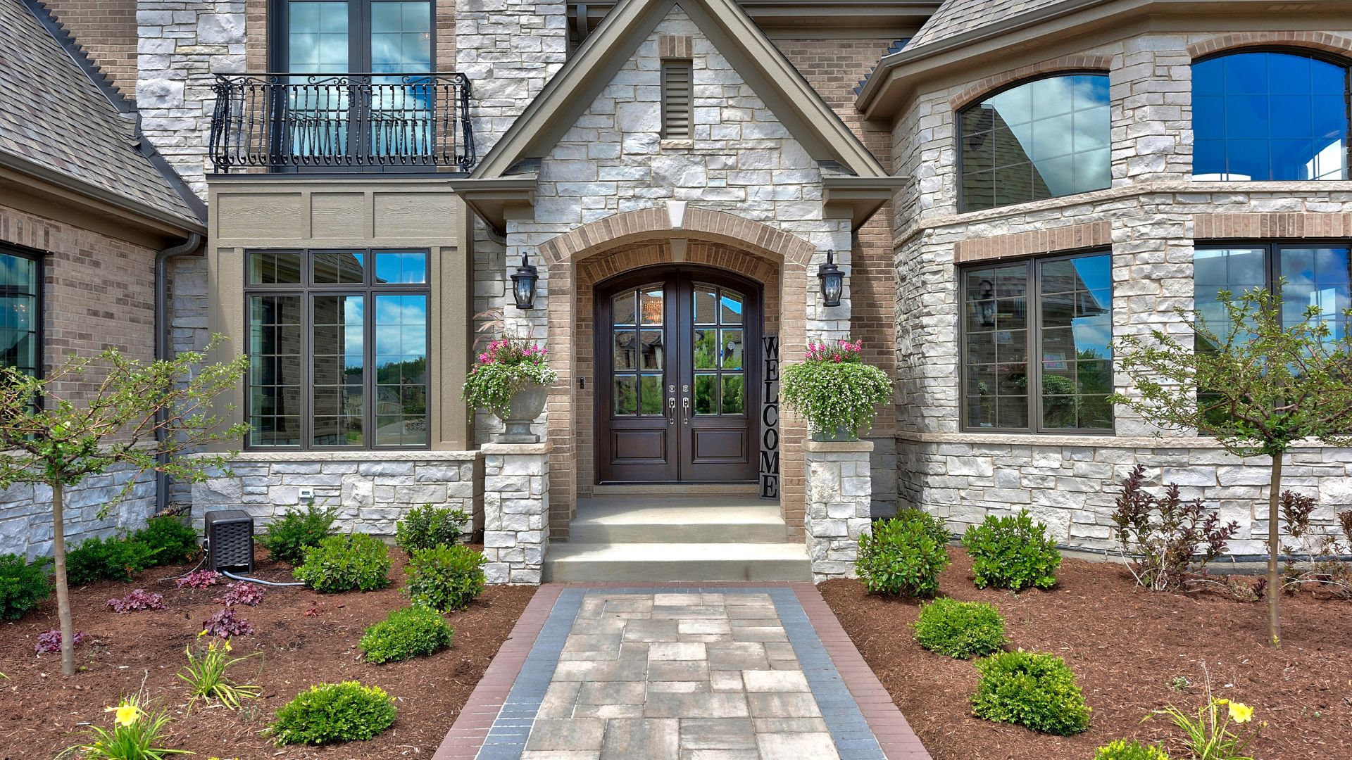 Modern stone house with arched entry door, manicured landscaping, and large windows.