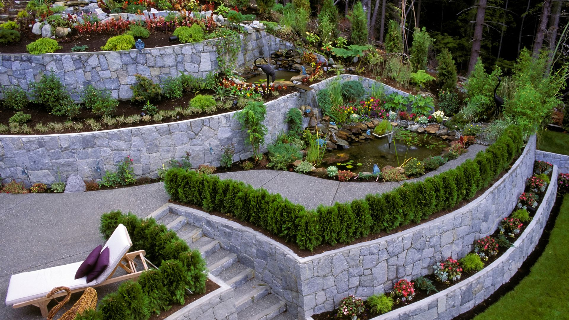 Terraced garden with stone retaining walls, ponds, plantings, and lounge chairs