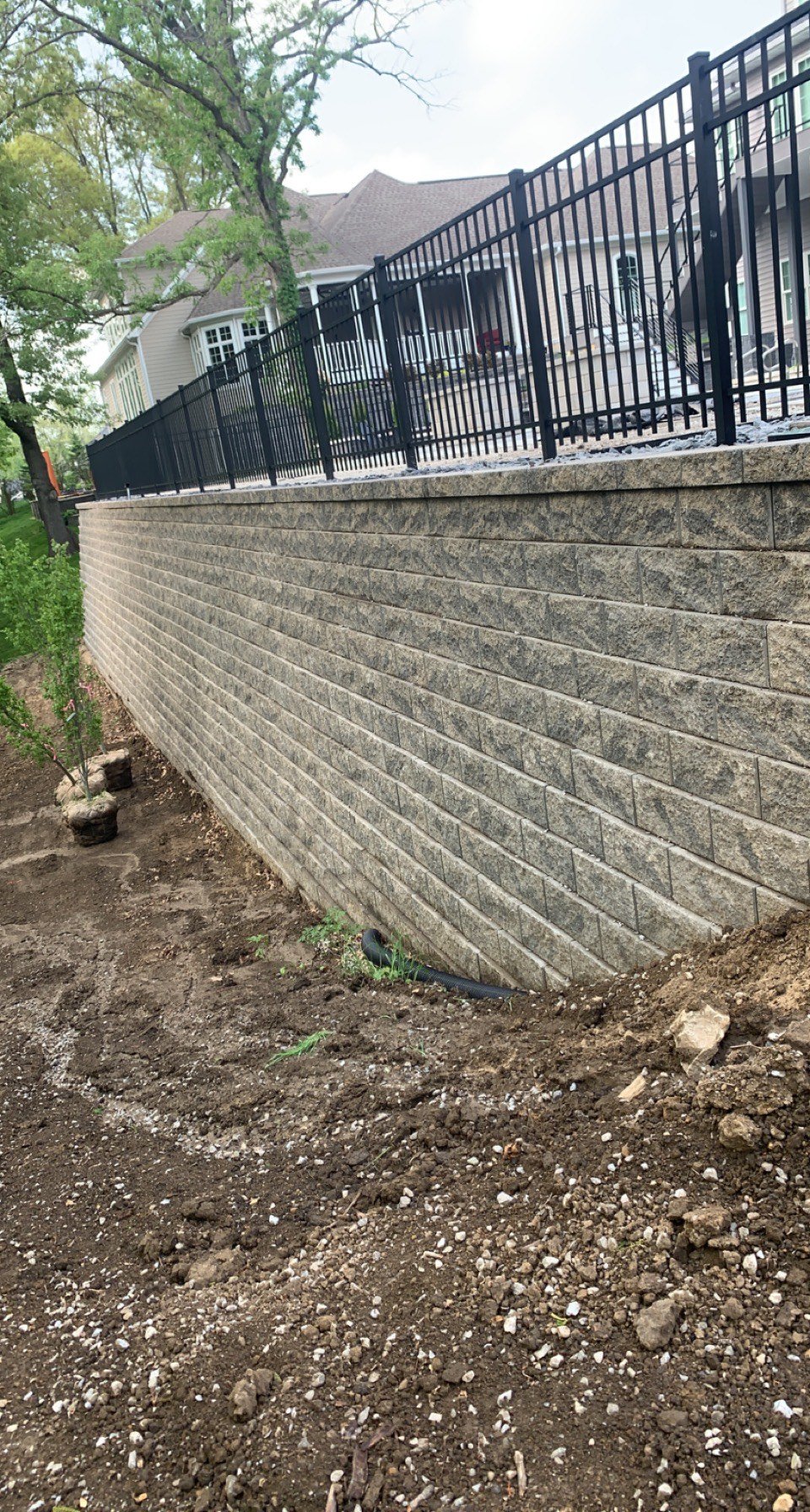 Retaining wall with black metal fence, unfinished landscaping around house