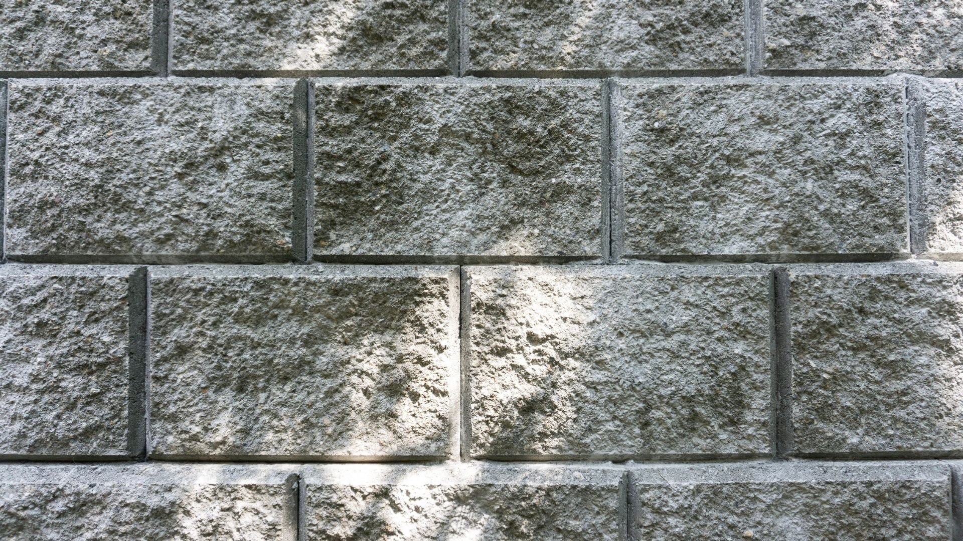 Textured gray concrete block wall with rough surface and shadow