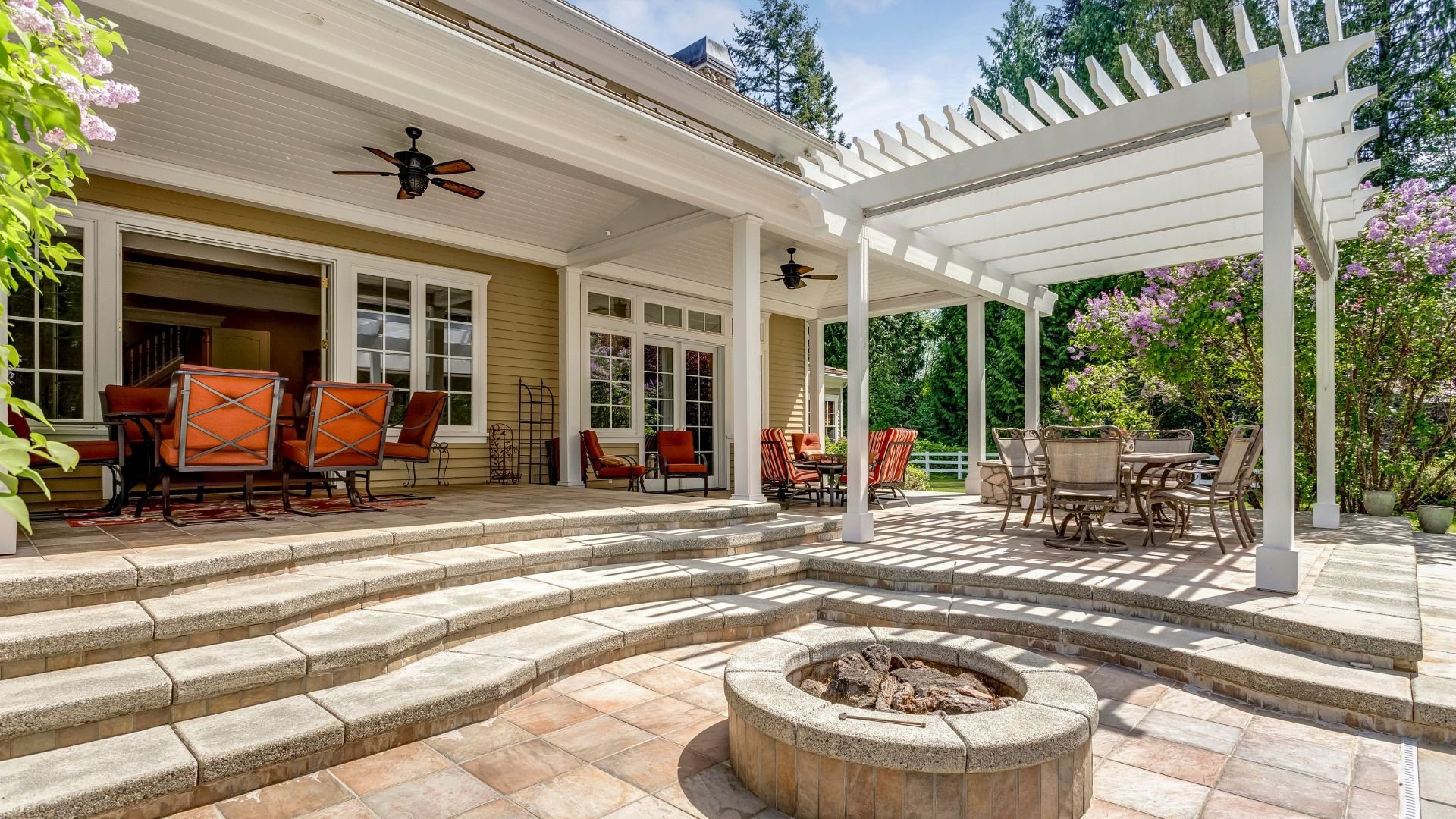 Luxurious outdoor patio with pergola, seating, and fire pit surrounded by trees